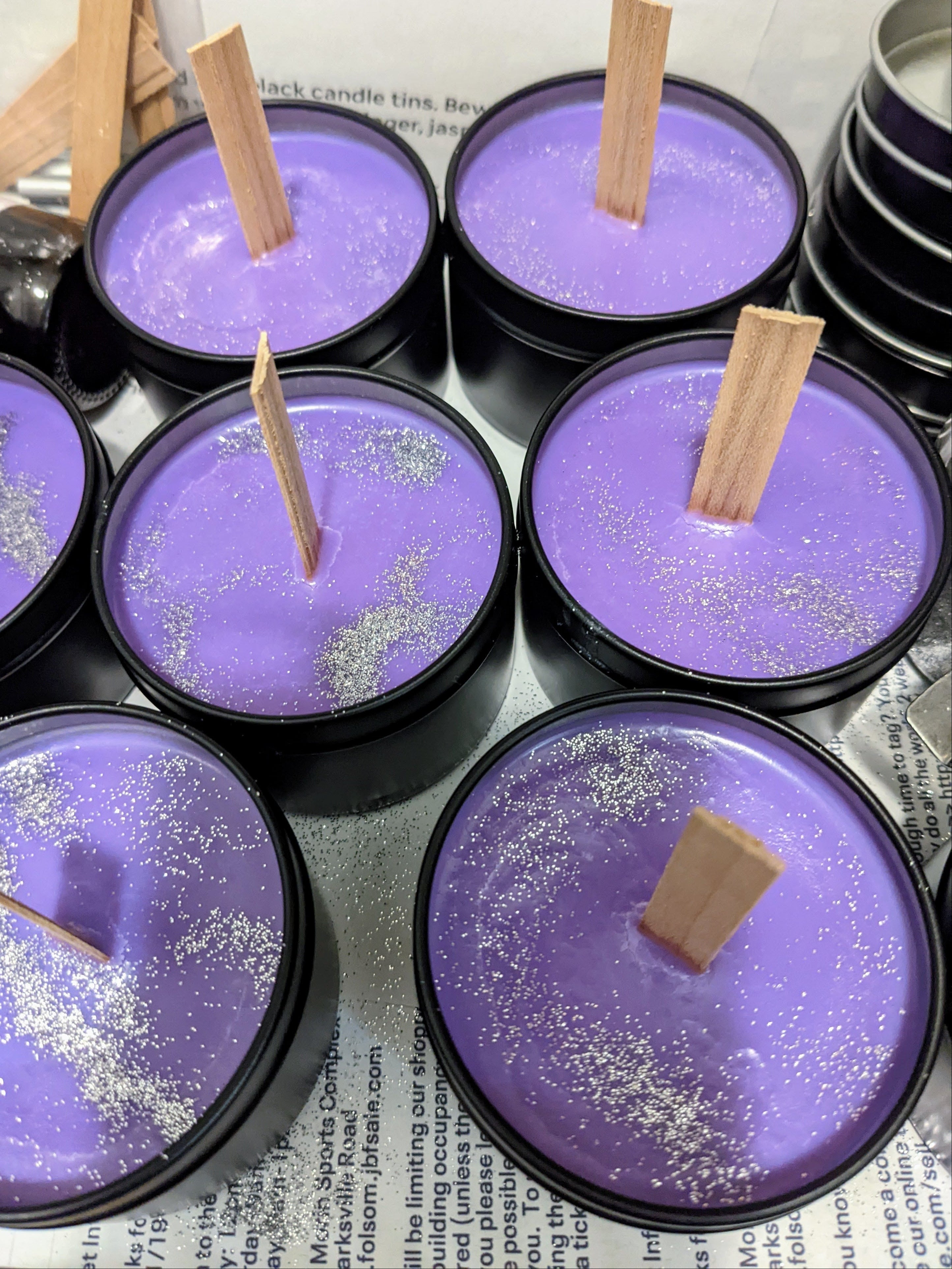 Purple candles with wooden wicks in black tins on a newspaper background